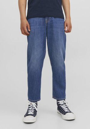 Jean en denim coupe régulière, de couleur bleu moyen, avec une jambe droite et des coutures visibles. Associé à des baskets en toile navy.