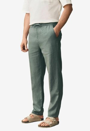 Light green linen pants with an elastic waistband, side pockets, and a relaxed fit, paired with beige sandals.
