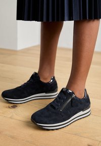 Baskets en suède noir avec une semelle à rayures blanches, dotées d'une fermeture éclair sur le côté, d'un bout rond et d'un design à lacets. Tige texturée et accents contrastants.