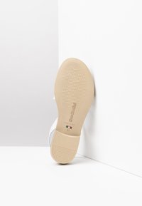 Suola in gomma color sabbia di una scarpa con un motivo di presa testurizzato. Parte superiore bianca in materiale sintetico con un design sottile e un indicatore di taglia 37.