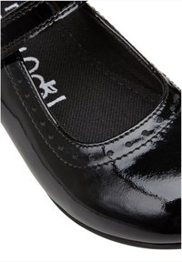 Scarpa in vernice nera con punta arrotondata e una fascia sul collo del piede. Presenta perforazioni decorative vicino al bordo e una soletta texturizzata.
