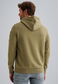 Olivově zelená mikina s kapucí, žebrovanými manžetami a lemem, s bočním kapsovým detail. Měkká tkanina s hladkým povrchem na zadní straně.