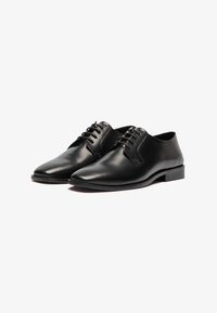 Zapatos de cuero negro con un diseño elegante, punteras afiladas y seis ojales para los cordones. Textura suave con detalles minimalistas.
