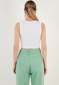 Witte cropped tanktop gecombineerd met lichtgroene wijde broek met achterzakken en een geplooide tailleband. Soepele stof, eenvoudig ontwerp.