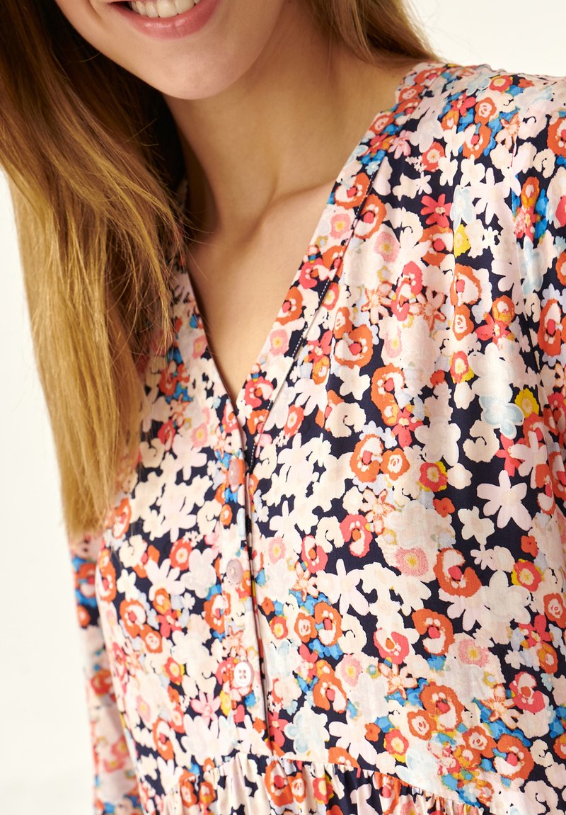 Blumenkleid mit V-Ausschnitt, das eine Mischung aus roten, rosa und blauen Blumen auf einem navy Hintergrund zeigt, aus leichtem Stoff gefertigt.