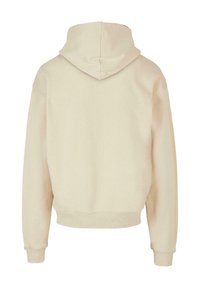 Beige kapucnis pulóver bordázott textúrával, laza illeszkedéssel, lecsúszott vállakkal és passzéval ellátott ujjal. Egyszerű és minimalista kialakítás.