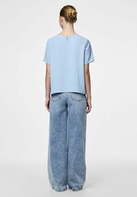 Ljusblå kortärmad topp med texturerad yta, med en nyckelhålsdetalj bak, parat med vida ljusblå denimjeans.