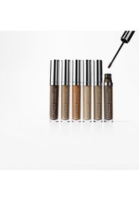 Zes tubes van Clinique wenkbrauwgel in verschillende tinten bruin. Elk heeft een doorzichtig lichaam en een zilveren dop. Eén tube is open, waarbij de borstelapplicator zichtbaar is.