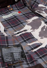 Cotton blend fabric with grey, red, and orange plaid pattern. Features cow illustrations and a care label in black.