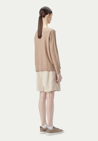 Stickad brun tröja med avslappnad passform, långa ärmar och rundad nederkant, kombinerad med en beige kjol och ljusbruna sneakers.