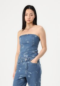 Ermeløs denim topper med blomstermønster, sammen med matchende jeans. Begge plagg viser et blått stoff med en subtil tekstur.