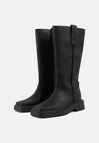 Botas negras hasta la rodilla hechas de cuero suave, con punta cuadrada, costuras cosidas, tiradores laterales y suela de goma gruesa.