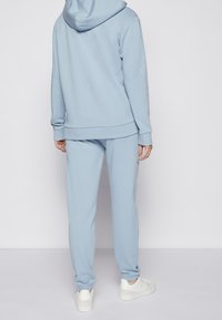 Sudadera de algodón azul claro con un ajuste regular, combinada con pantalones joggers a juego. Presenta un bolsillo tipo canguro en la parte frontal y puños acanalados.