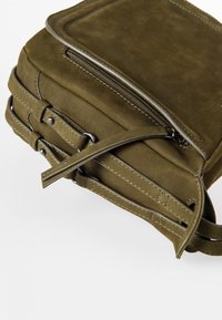 Olivgrüne Wildleder-Umhängetasche mit Reißverschluss oben, flachem Design, gesteppten Akzenten, verstellbarem Riemen und glatter Textur.