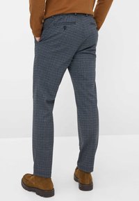 Pantaloni a quadri grigi realizzati in tessuto intrecciato, con un taglio dritto, tasche posteriori con bottone, abbinati a scarpe in suede marroni.