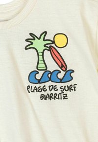 Palmier, soleil jaune, planche de surf rouge, vagues bleues de l'océan, et texte "PLAGE DE SURF BIARRITZ" sur tissu blanc.