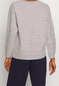 Sudadera gris con tejido texturizado, mangas raglán y dobladillo acanalado. Presenta un diseño liso sin ninguna marca o patrón visible.