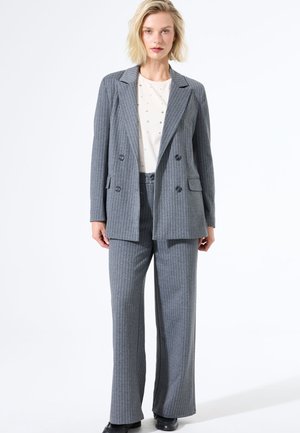 Ensemble de blazer et pantalon à rayures grises, coupe ajustée, blazer croisé, pantalon à devant plat, associé à un top crème avec de petites embellissements.