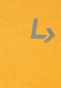 Żółta dzianina z szarym graficznym symbolem "L" i strzałką w prawo, podkreślająca poziome ułożenie i teksturowaną powierzchnię.