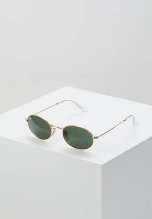 Occhiali da sole in metallo dorato con lenti ovali verdi, aste metalliche sottili e punte trasparenti. Le montature presentano un design minimalista e arrotondato.