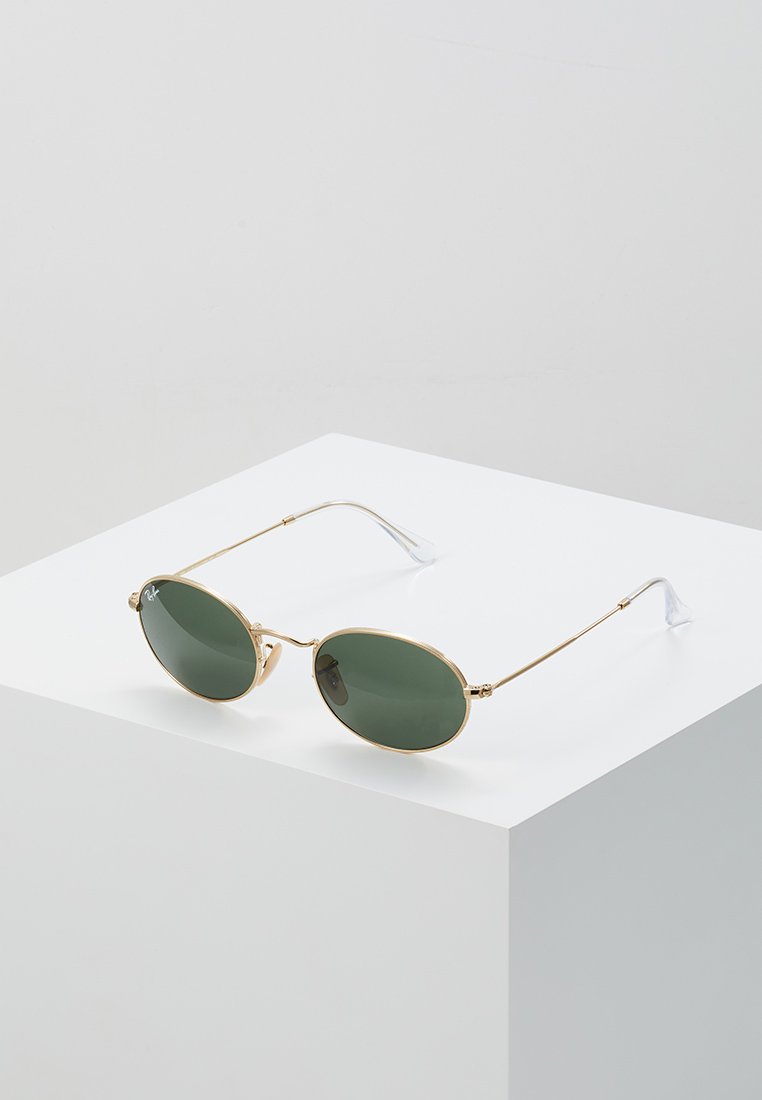 Occhiali da sole in metallo dorato con lenti ovali verdi, aste metalliche sottili e punte trasparenti. Le montature presentano un design minimalista e arrotondato.