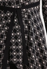 Svart och vit mönstrad tyg med geometriska cirkulära mönster, som har ett helt svart midjebälte knutet i en lös knut.