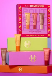 Conjunto de cuatro cajas coloridas que exhiben mini tratamientos labiales en tubos naranja, rosa y marrón; apiladas sobre un fondo rosa.