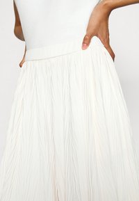 Plisserad vit kjol med elastisk midja, som har ett lätt tyg med en mjuk, texturerad yta och ett flödande design.