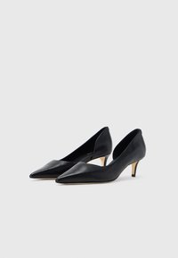 Musta nahkainen, teräväkärkinen kenkä, joka on matalalla piikkikorolla. Sileä pinta ja tyylikäs siluetti, jossa on leikkaukset sivuilla koristeena.