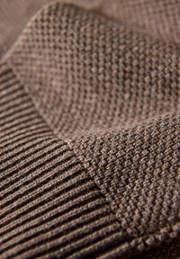 Brązowa tkanina z dwoma fakturami: gładka, żebrowana część oraz wzór tkany, tworzące wizualny kontrast materiału i wzoru.