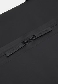 Černá taška Calvin Klein s texturovaným povrchem, výrazným zipem aznačkovaným táhlem zipu pro bezpečný přístup.