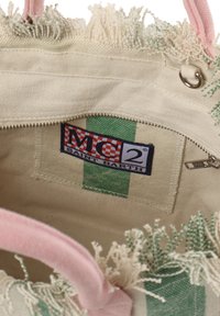 Innenansicht einer Canvas-Tasche mit grünen und weißen Streifen, einem pinken Griff, fransigen Kanten und einer Reißverschlusstasche mit einem Logo-Anhänger.