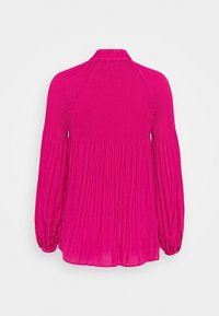 Fuchsia långärmad topp med hög krage, texturerat ribbad tyg och veckade detaljer bak som ger en flödande silhuett.