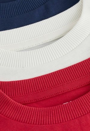 Drei Crewneck-T-Shirts übereinander gestapelt: marineblau, creme und rot. Jedes Shirt hat gerippte Kragen und ein glattes Baumwollgewebe, das lebendige Farben zeigt.