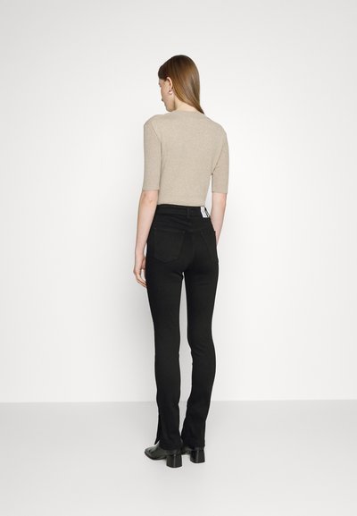 Calças de ganga pretas elásticas com cintura alta e pernas largas, combinadas com uma blusa ajustada bege, exibindo um design e textura limpos.