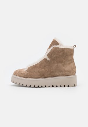 Beżowy zamszowy botek za kostkę z miękkim futerkiem w środku i jasną, grubą podeszwą. Posiada zaokrąglony czubek oraz pętlę do zakładania z tyłu.