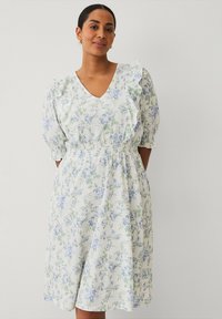 Robe florale avec un fond blanc ornée de motifs bleus et verts, des manches bouffantes courtes, un décolleté en V et une taille élastique.