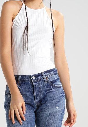 Witte geribbelde haltertop gecombineerd met versleten blauwe spijkerbroek met een hoge taille en lichte vervaging. Eenvoudig ontwerp met minimale accenten.