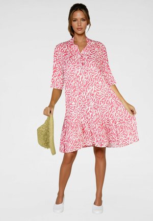 Robe chemise à motifs rose et blanc avec un ourlet évasé, des manches trois-quarts et un col à boutons ; associée à un chapeau de paille.