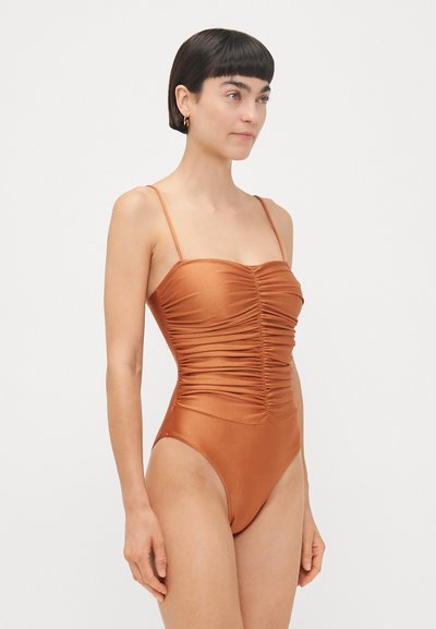 Rust-colored one-piece swimsuit with thin adjustable straps, featuring a ruched design at the bust and a high-cut leg. Smooth texture.