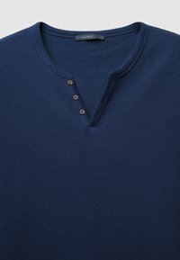 Chemise Henley à manches longues bleu marine en tissu texturé, avec un col en V et trois boutons marron près du col.