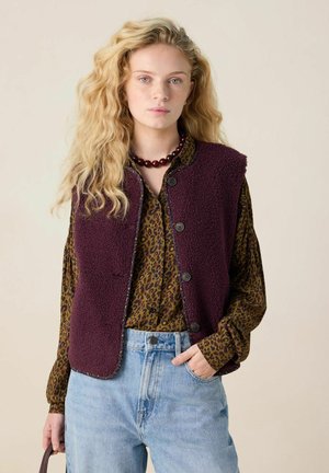Burgunderfarbene Fleece-Weste mit Rundhalsausschnitt, vorderen Knopfverschlüssen und kontrastierenden Stichdetails, getragen über einem braunen Leopardenmusterhemd.