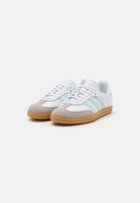 Weiße und graue Sneakers mit mintgrünen Streifen, samtigem Zehenbereich, Gummisohle und Schnürdesign. Mit Branding an der Seite.