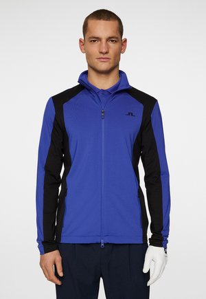 Blue and black zip-up jacket with a mock collar, featuring long sleeves and a logo on the chest. Made from a lightweight, stretchy material.