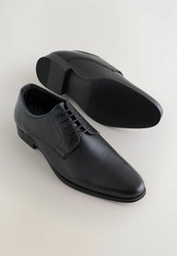 Sorte dressko med en struktureret læderoverdel, rund tå og snørebåndsdesign. Har en glat sål og minimalistisk stil.