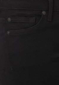 Primer plano de unos jeans de mezclilla negra que muestra el bolsillo frontal, el bolsillo para monedas, el pasador del cinturón y los remaches de metal.