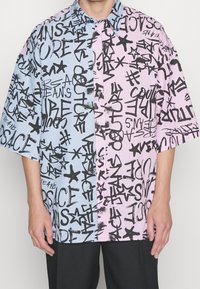 Camisa de botones de manga corta con un diseño dividido en azul claro y rosa, con texto en negrita estilo graffiti en negro y acentos de estrellas.