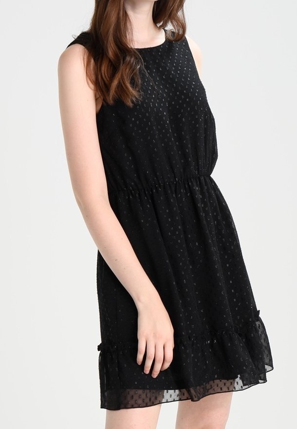 Robe noire sans manches avec un col rond, taille élastique et ourlet à volants. Fabriquée dans un tissu doux et texturé avec des pois subtils.