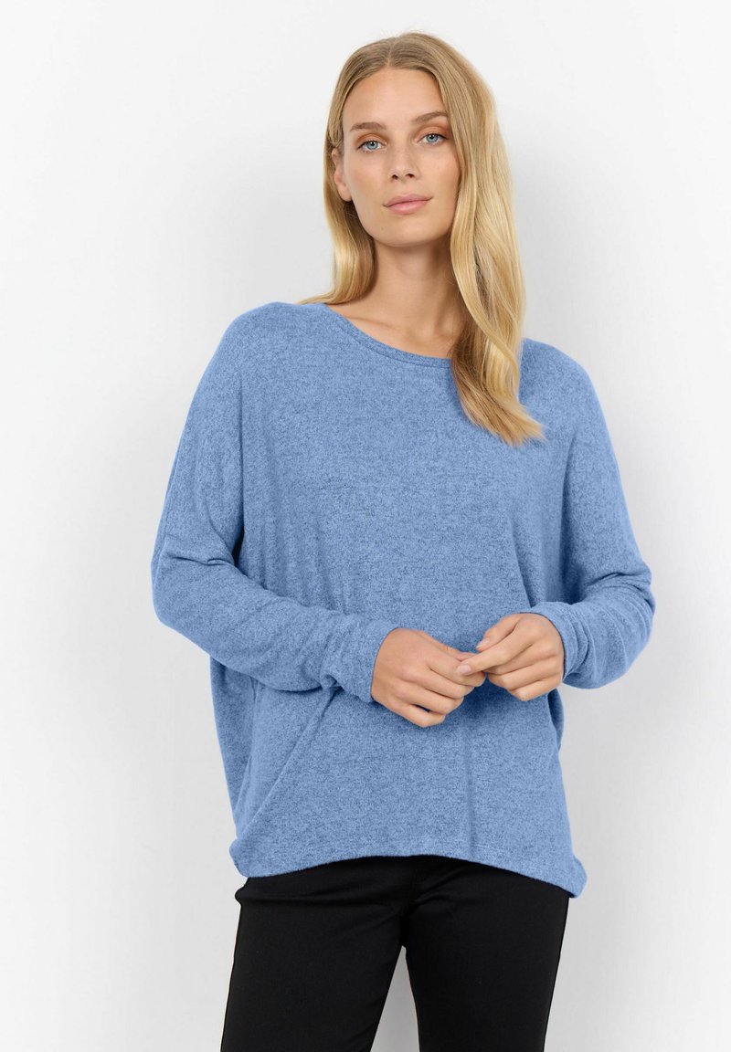 Helles blaues, übergroßes Sweatshirt mit langen Ärmeln, aus weichem Stoff gefertigt, mit rundem Hals und lockerer Passform. Kombiniert mit schwarzen Hosen.