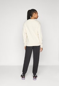Kremet sweatshirt med ribbestrikkede mansjetter, kombinert med svarte joggebukser og svarte sneakers med rosa detaljer, sett fra baksiden.